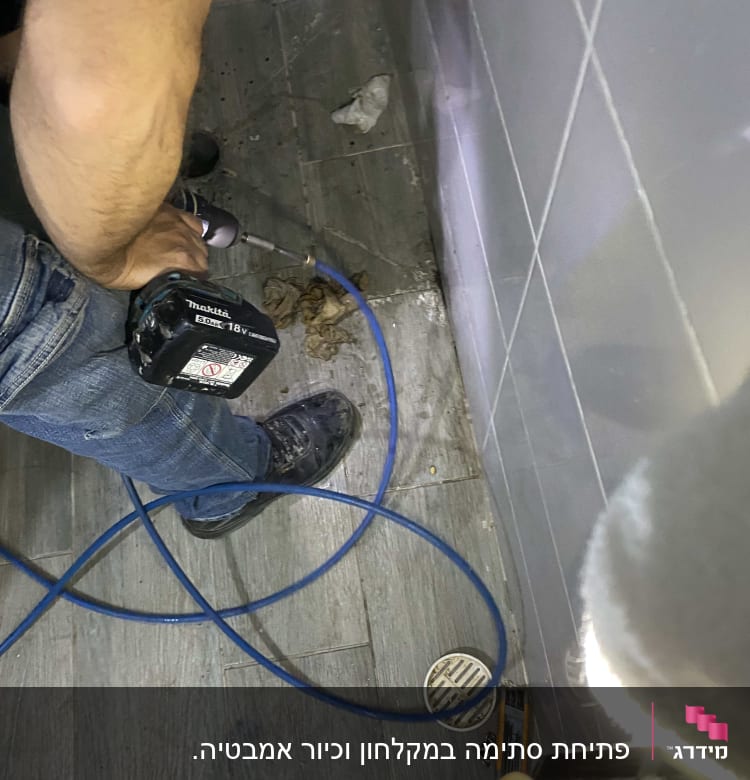 אדם משתמש במקדחה ליד ניקוז רצפה